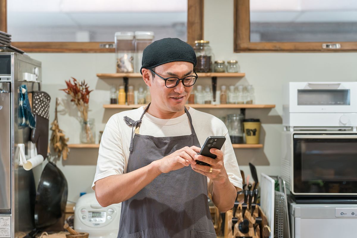 厨房でスマートフォンを操作するエプロン姿の男性