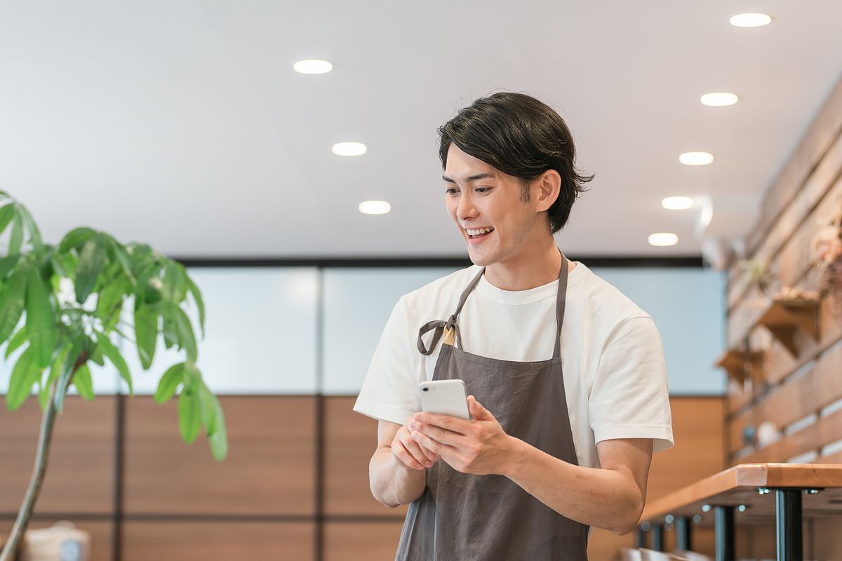 店内でスマートフォンを見て微笑む男性従業員